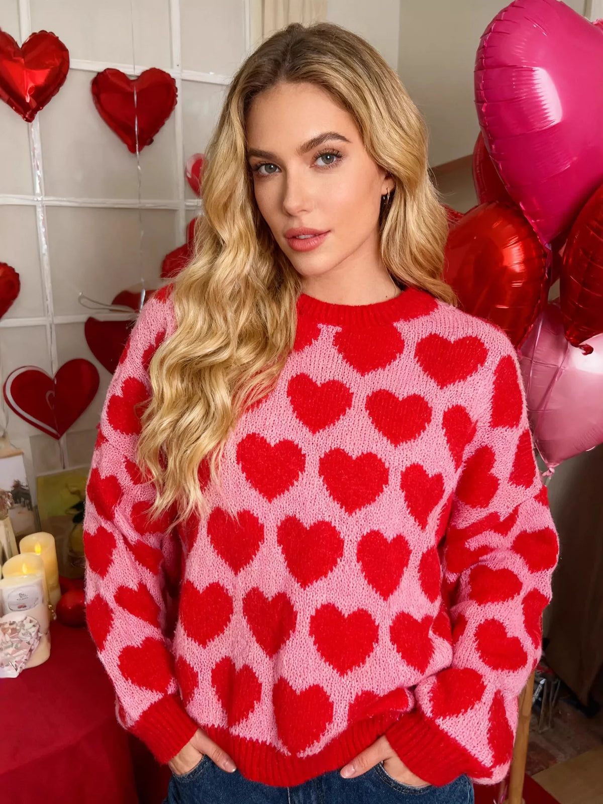 Model wearing a pink sweater with red hearts and red ribbed trim, styled with blue jeans.