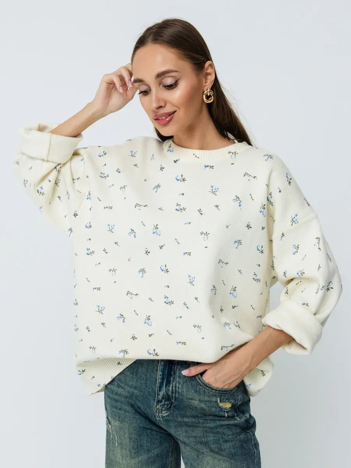 Model wearing a cream oversized sweater with a small floral pattern and blue jeans.